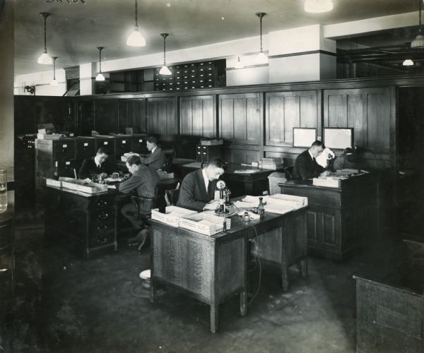 Workers sitting at desks in the offices of Harvester Press, International Harvester's in-house print shop.
