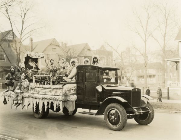 International Model S speed truck carrying reindeer and men dressed as clowns, Eskimos, and Santa Claus during a winter parade. A blanket on reindeer reads: "From Kringleland to the fair."