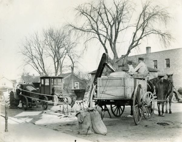 Farmer and boy grinding feed with a McCormick-Deering belt-driven feed grinder and an International 8-16 tractor. Parked nearby are an International truck and an unidentified horse-drawn wagon.