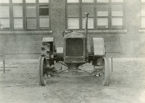 Experimental McCormick-Deering 15-30 tractor parked outside a brick building (possibly International Harvester's Tractor Works in Chicago).  This photograph was taken by International Harvester's engineering department. The original caption reads: "15-30 wide tread tractor with short turn steering device - front view."