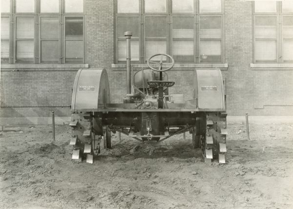 Experimental McCormick-Deering 15-30 tractor parked outside a brick building (possibly International Harvester's Tractor Works). This photograph was taken by International Harvester's engineering department. The original caption reads: "15-30 wide tread tractor with short turn steering device - rear view."