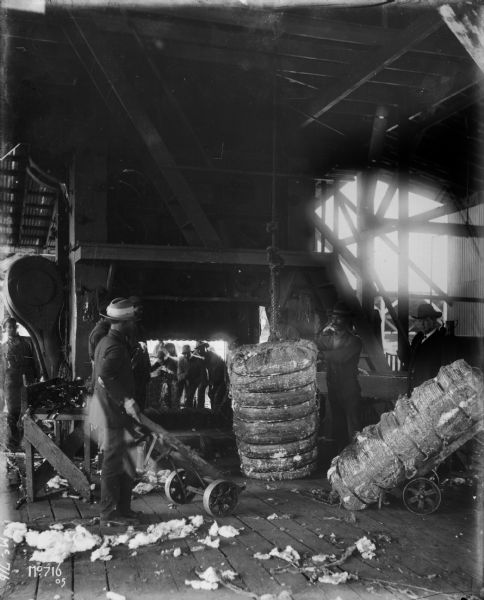 African American workers unloading bales of cotton inside a warehouse building.