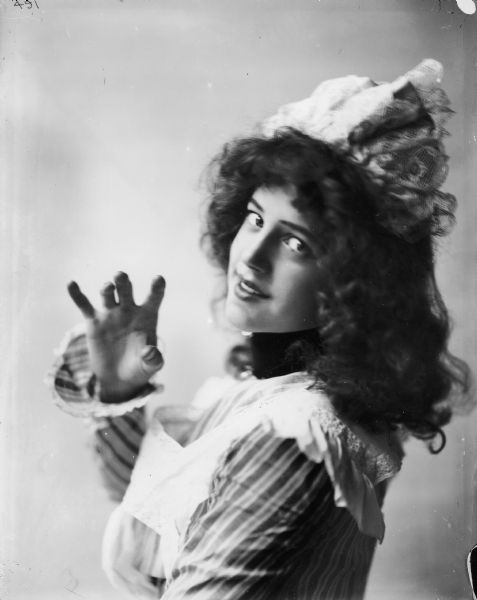Waist-up portrait of a woman dressed as a "dairy maid"(?) posing as if holding an imaginary cup or glass. The image was most likely used as a model for a color advertising illustration or calendar.