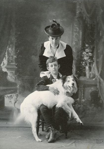 Family studio portrait of Anita McCormick Blaine (1866-1954), her son, Emmons Blaine, Jr. (1890-1918), and a family dog. They are posing in front of a painted backdrop.