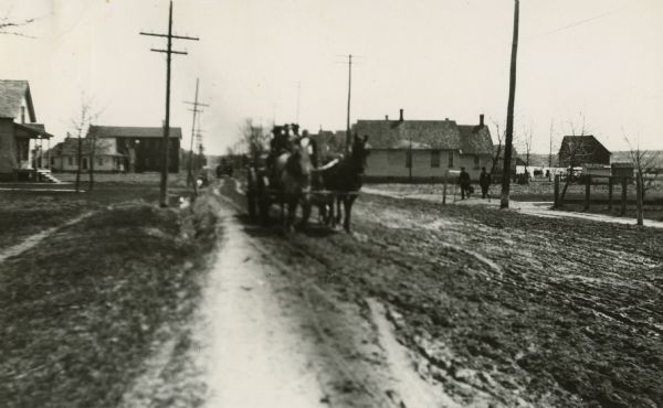 Horse-drawn wagon on Cedar Creek Road in Brown County. The road is dirt and there are houses in the backgound.