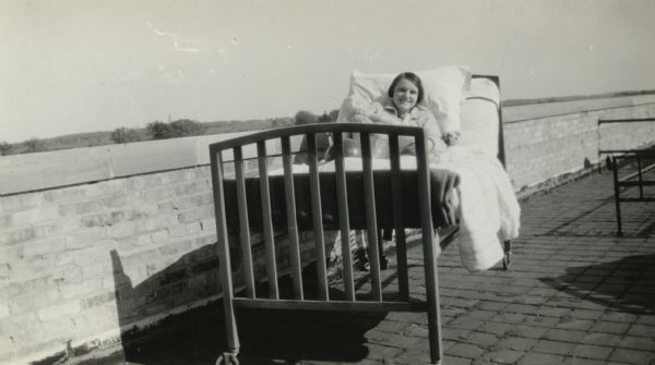 Young tuberculosis patient sitting up in bed. The bed is on an outdoor porch.