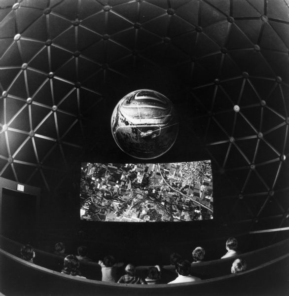 People watching a program in the "Agrisphere," an 80-capacity theater in a 40-foot-high geodesic dome in the Chicago Museum of Science and Industry paid for by International Harvester. In the theater there is an 18-foot screen, and above that is an "Earthscape", which depicts the U.S. landscape as it changes from early time to modern day, using a three-dimensional effect.