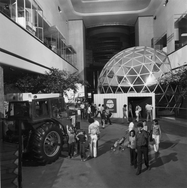 Men, women and children walk through the Harvester Farm exhibit at the Museum of Science and Industry. The exhibit included a tractor and the "Agrisphere", a theater in the shape of a sphere.