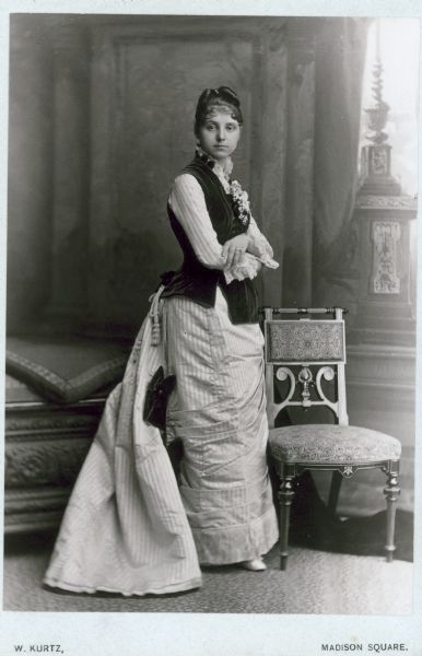 Portrait of Mary Virginia McCormick (1861-1941) as a young woman. Mary Virginia was the daughter of Chicago industrialist and inventor, Cyrus Hall McCormick. She is wearing a long gown with a bustle, and is standing beside a chair.
