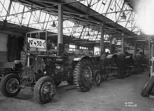McCormick F-12-G tractors on an assembly line at International Harvester's Neuss Works (factory) in Germany. The first tractor is decorated with fir tree boughs.