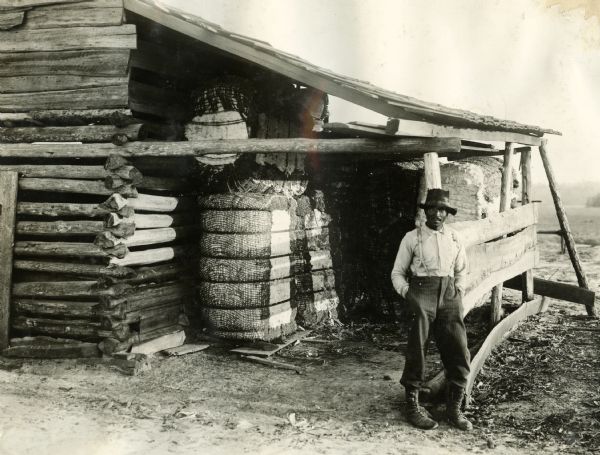 Farmer L.C. Carter standing beside bales of cotton and a farm building.