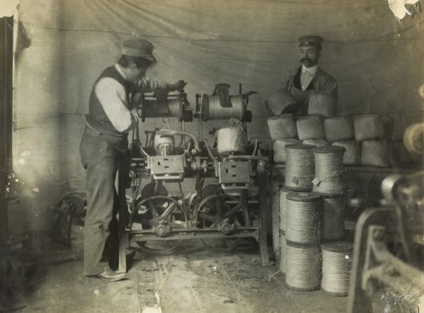 A man operates a balling machine while another handles spools of binder twine. The men may have been working at the McCormick twine mill in Chicago.