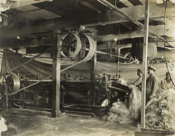 Men in a factory comb fiber (fibre), the first process preparatory to spinning. International Harvester used sisal fiber to make binder twine. The men may be workers at International Harvester's McCormick twine mill in Chicago, Illinois.