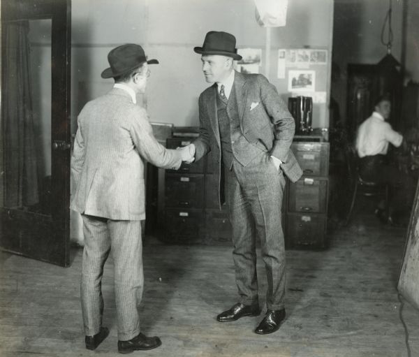 Businessmen Starbuck and Hayne shaking hands in an office setting.