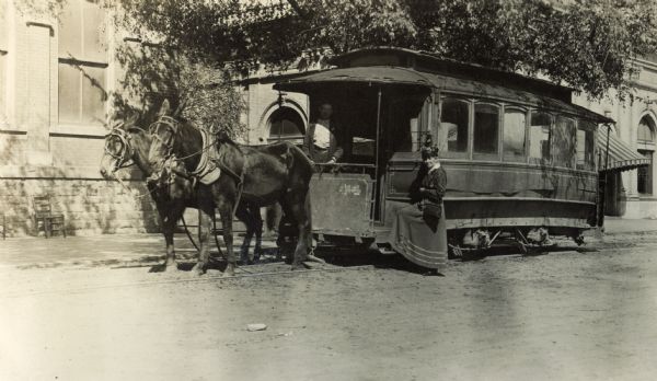 Mrs. Howie standing beside a horse-drawn streetcar of the Covington Line. The car is manned by a conductor.