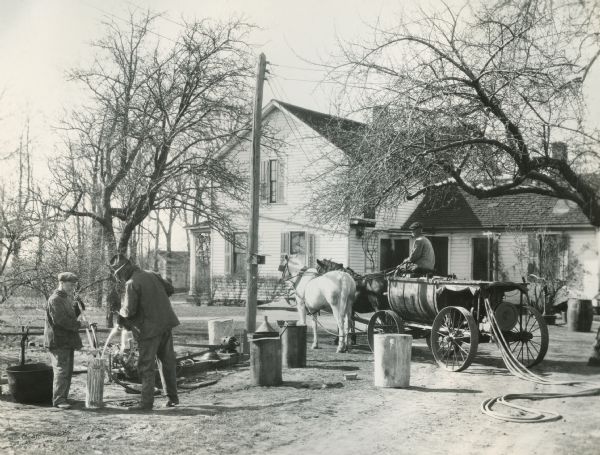 Two men mixing arsenate of lead before starting out for the orchard on R.R. Roberson's farm. A man on a McCormick-Deering 15-30 tractor and sprayer is looking on.