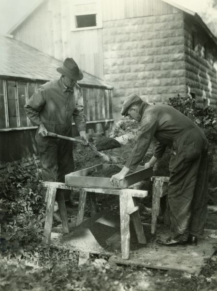 Two men sifting compost soil through a screen.