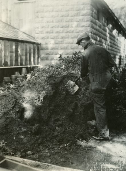 A man cutting down a compost pile with a shovel.
