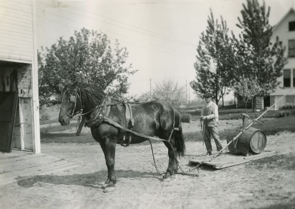 A man is using a horse to pull a barrel sprayer on a drag at Prof. Holden's farm.