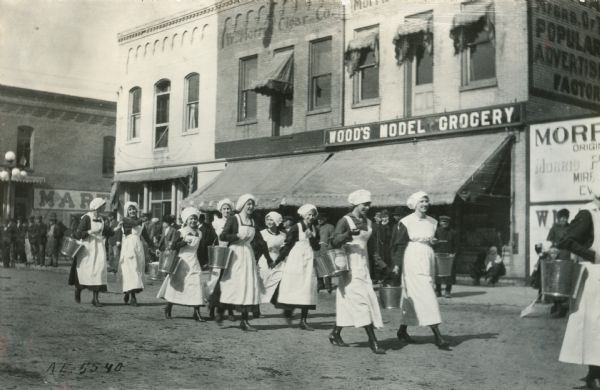 "Dairy maids" walk down the street in front of Wood's Model Grocery in "the big parade."