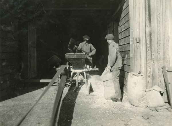 Two young men working with a feed grinder on Claus Johnson's farm.