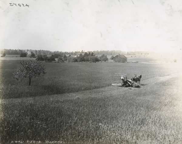 A farmer uses a horse-drawn Deering grain binder in a field.