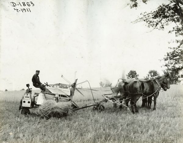 A farmer uses a Deering(?) grain binder pulled by four horses.