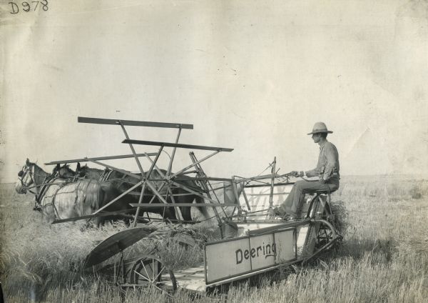 A farmer operates a Deering grain binder driven by four horses.