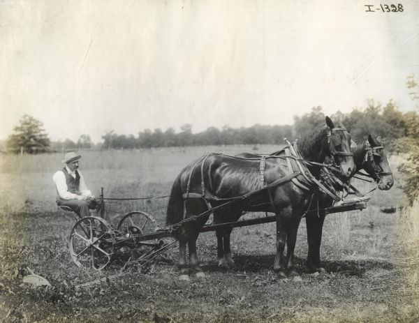 A man sits on a horse-drawn mower.