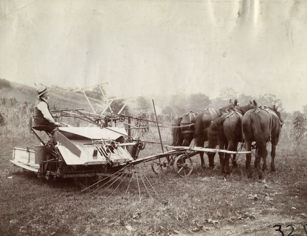 A farmer drives a team of four horses pulling a Champion grain binder.