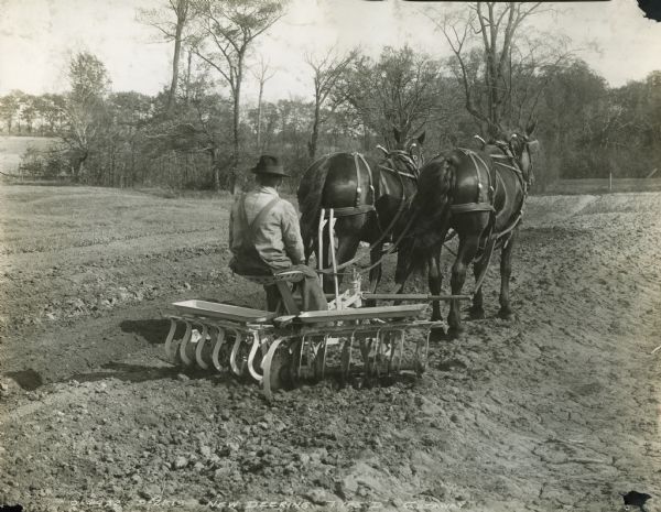 Rear view of a farmer using a horse-drawn Deering Type D disc harrow in a field.