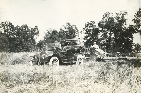 Men using a Buick automobile to pull a grain binder in a field, possibly to or from a photo shoot.