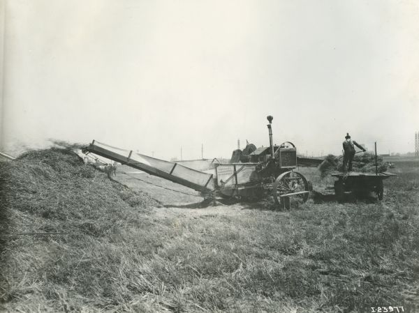 A farmer feeds grain from a wagon into a thresher.