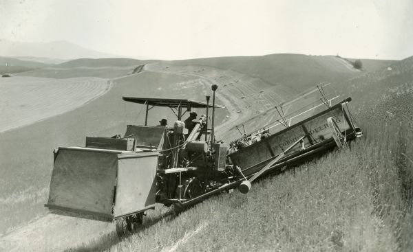 View from rear of J.P. Wedin operating a tractor and harvester-thresher (combine), sold by dealer L.C. Martin, along the side of a steep hill.