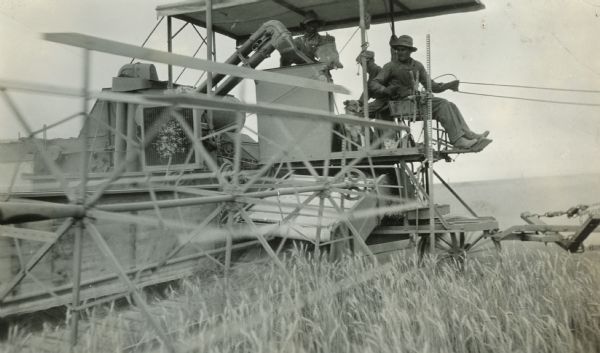 Theo Klemmer using a harvester-thresher (combine) sold by the Lind Hardware Company. Two other men are on the combine with him.