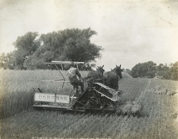 A farmer operates a horse-drawn Osborne grain binder through a field. The original caption reads: "Emerson-Brantingham."