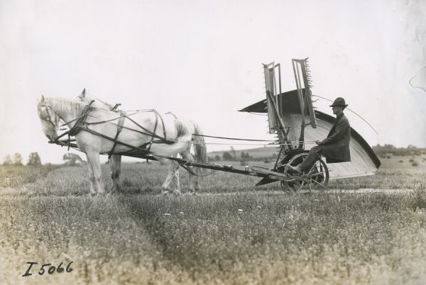 A farmer with a team of horses is driving on a road between fields with his reaper folded upright for transport.