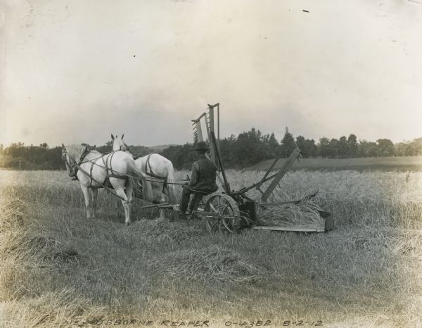 Farmer operating a horse-drawn Osborne reaper. The original caption reads: "Emerson-Brantingham."