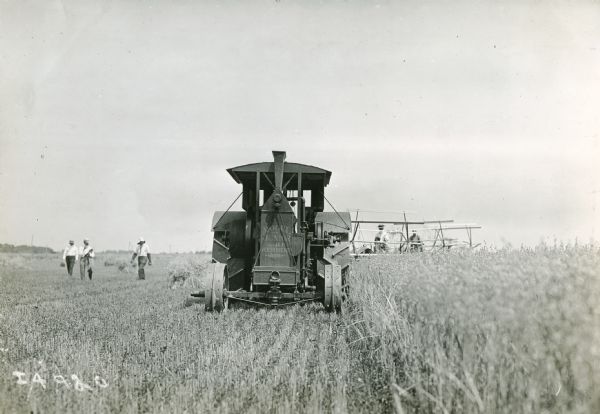 Mogul Junior tractor pulls several grain binders while men walk alongside.