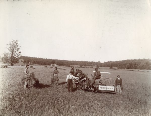 Five men pose for a photograph around a McCormick grain binder in a field.