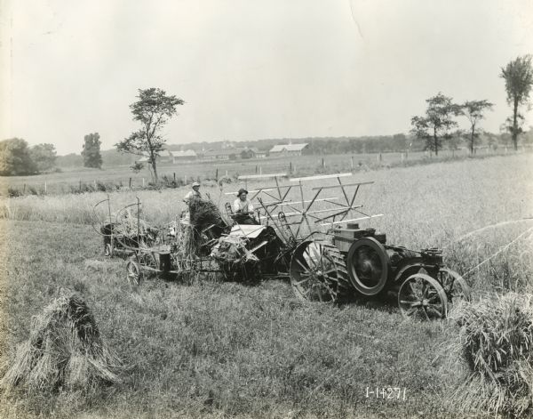 Two men using an experimental rig to operate a grain binder and a Mogul 8-16 tractor. Bundles of the harvested grain are stacked in the foreground.