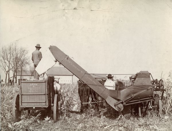 Two farmers operating a McCormick corn picker and wagon.