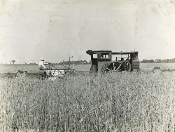 View across field towards a man sitting on a grain binder pulled by a Mogul tractor.