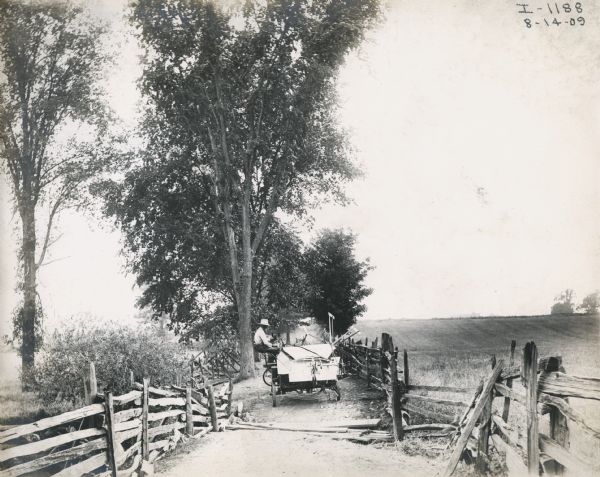 A farmer rides on a grain binder as it is transported down a country road by a pair of horses.