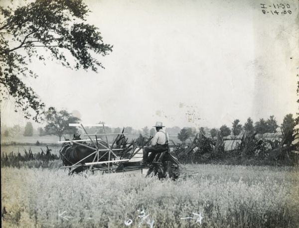 A farmer operating a McCormick grain binder in a field.