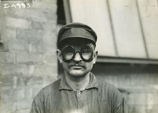 A man, possibly an International Harvester factory worker, poses for a photograph wearing eye protection goggles.