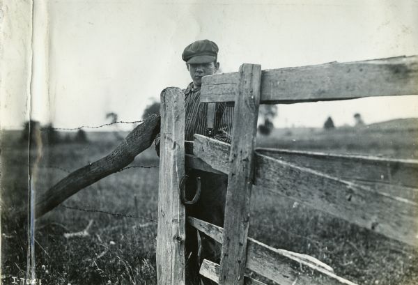 A boy stands behind a fence post with a horseshoe attached to it.