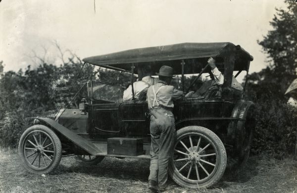 Several men sit inside an automobile while another stands nearby, looking in.