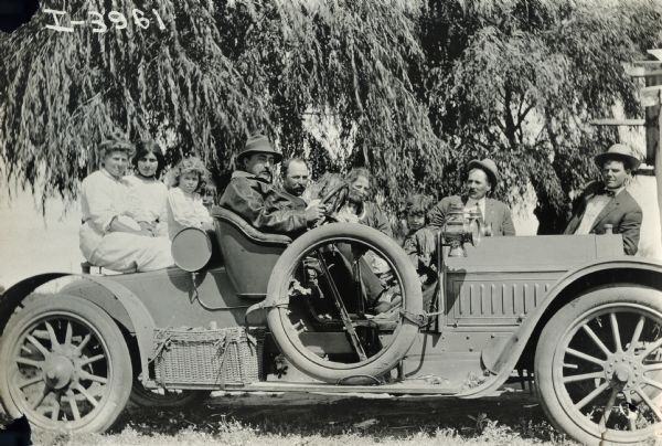 A group of men, women, and children pose for a portrait while seated in an automobile.
