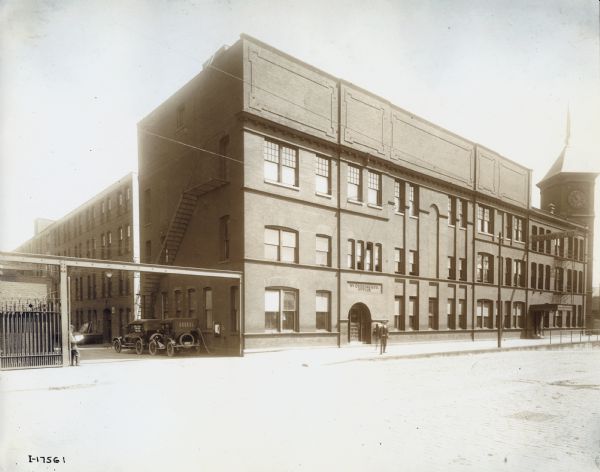 Exterior view of the Fullerton Avenue side of the Deering Works (factory) building. Two cars are parked just inside the factory gate. Before 1902, the building was operated by the Deering Harvester Company.